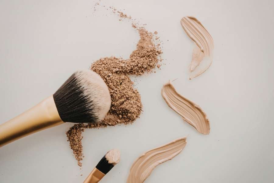 Des pinceaux de maquillage posés sur une surface claire avec de la poudre et du fond de teint.